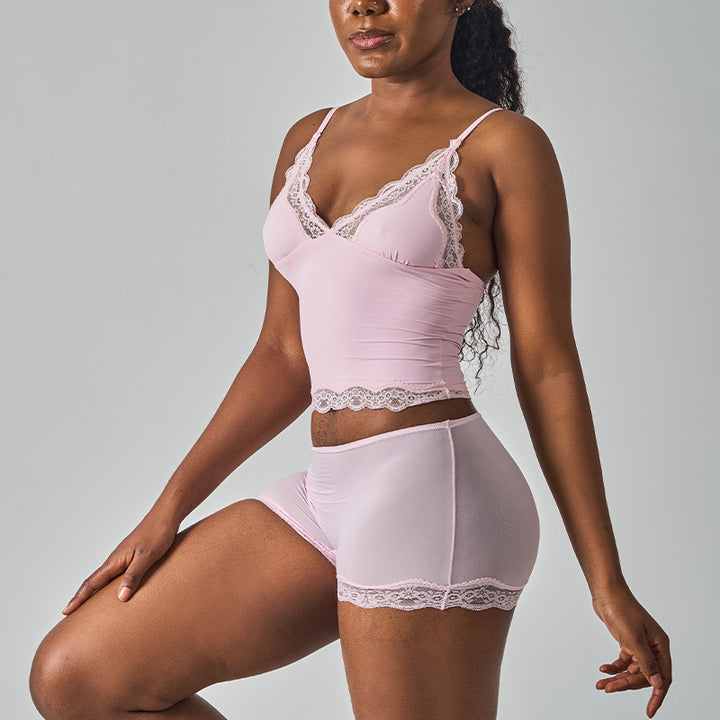 Woman wearing silky deep V-neck camisole and matching shorts in neutral tone, relaxed pose against minimal background