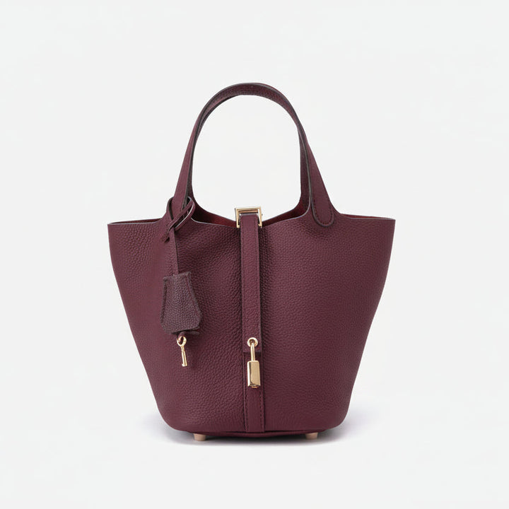 Burgundy structured basket handbag with metallic twist-lock clasp and faux-leather finish, held against neutral background
