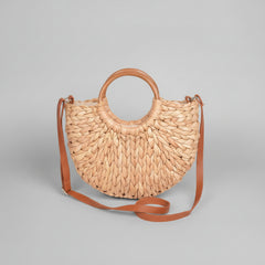 Natural straw clutch bag with sculptural twist knot detail, structured silhouette held against neutral background