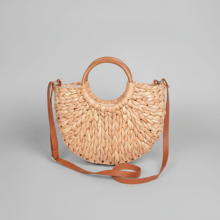 Natural straw clutch bag with sculptural twist knot detail, structured silhouette held against neutral background